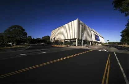 Modern white building with tall vertical slats on a wide street under a clear blue sky.